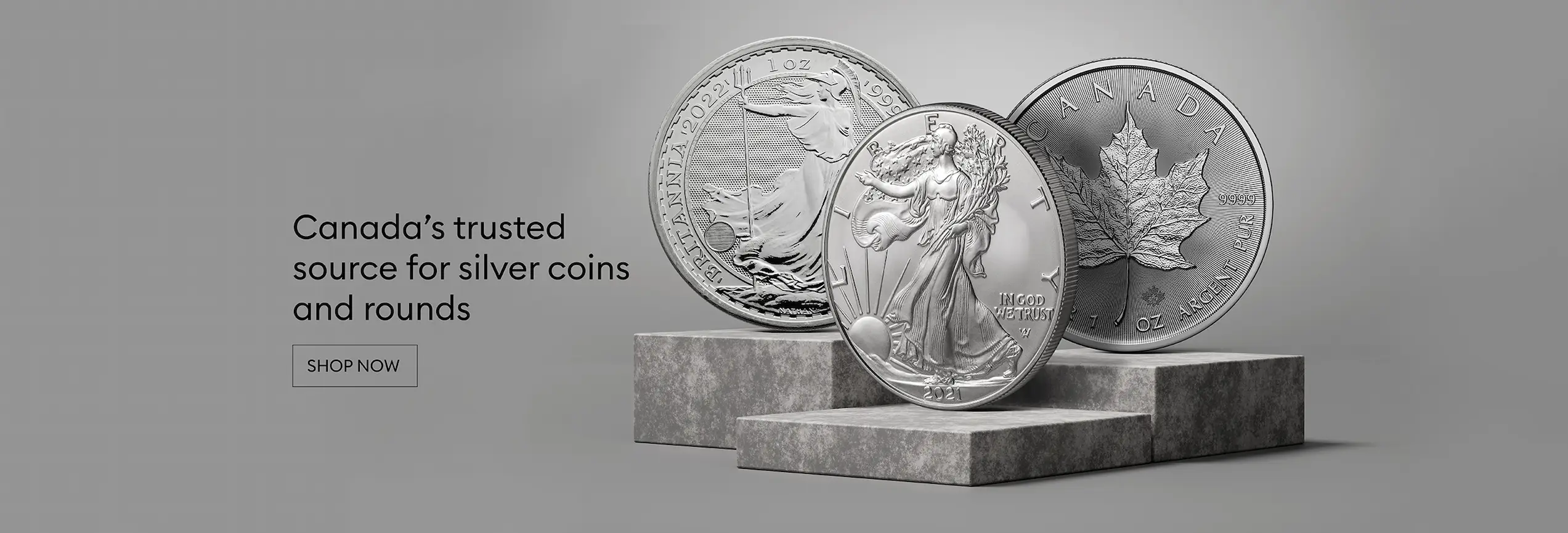 A canadian maple, brittania and  U.S. eagle silver coins on top of a podium. Plain Grey background.